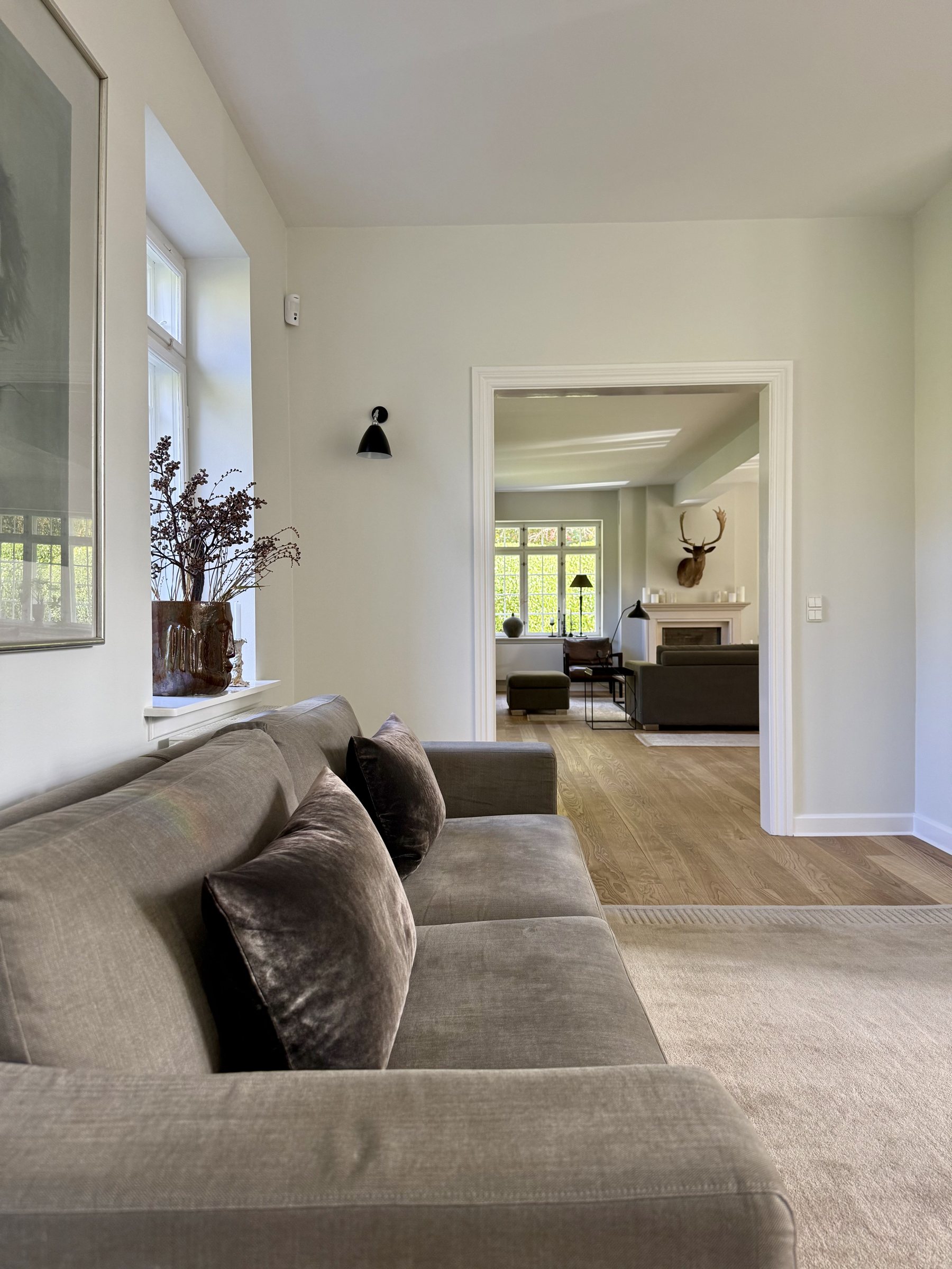 Sunlit sitting room opening through a classical doorway to the living room with fireplace