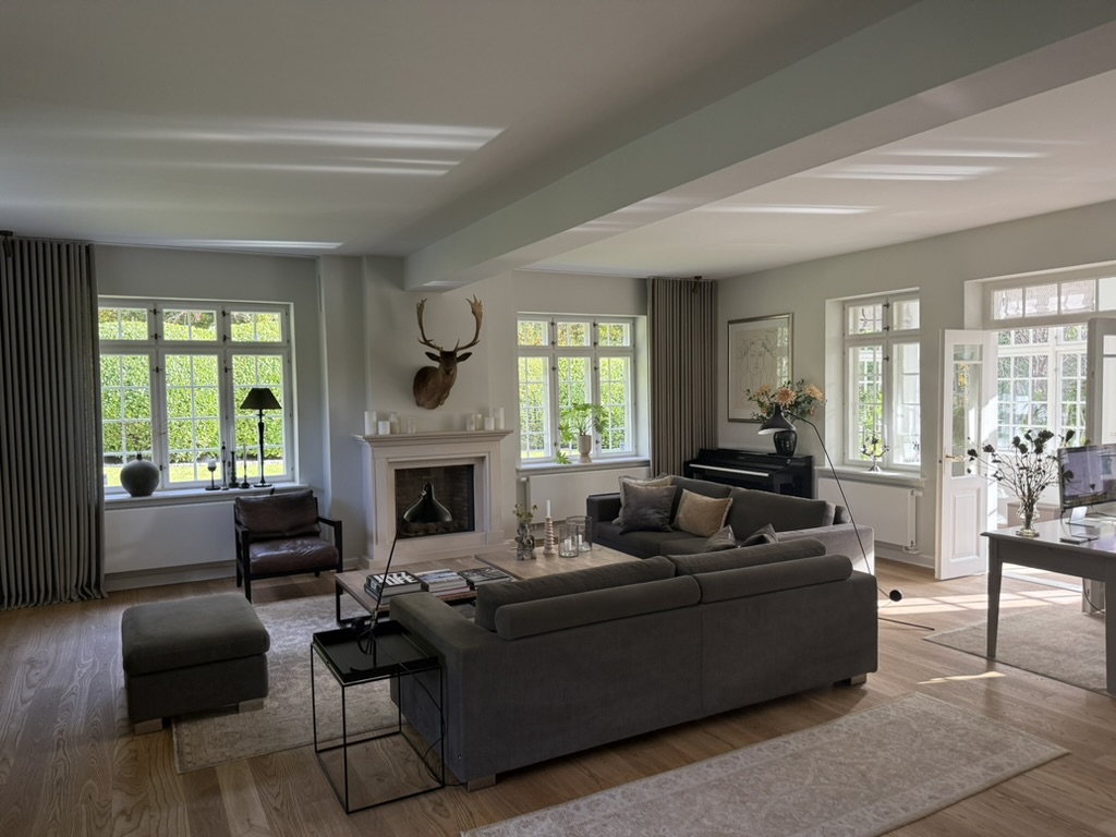 Living room with fireplace, tall paned windows and soft afternoon light across oak floors