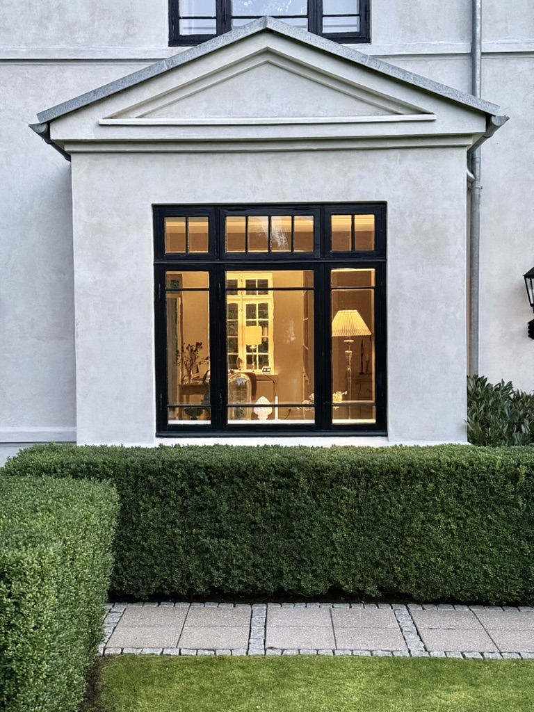 Pedimented bay window glowing at dusk above a clipped box hedge