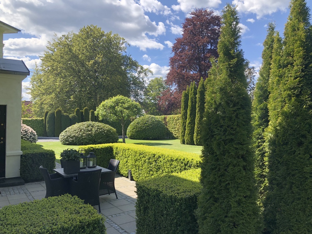 A terrace beside the house, framed by sculpted hedges, topiary and tall conifers